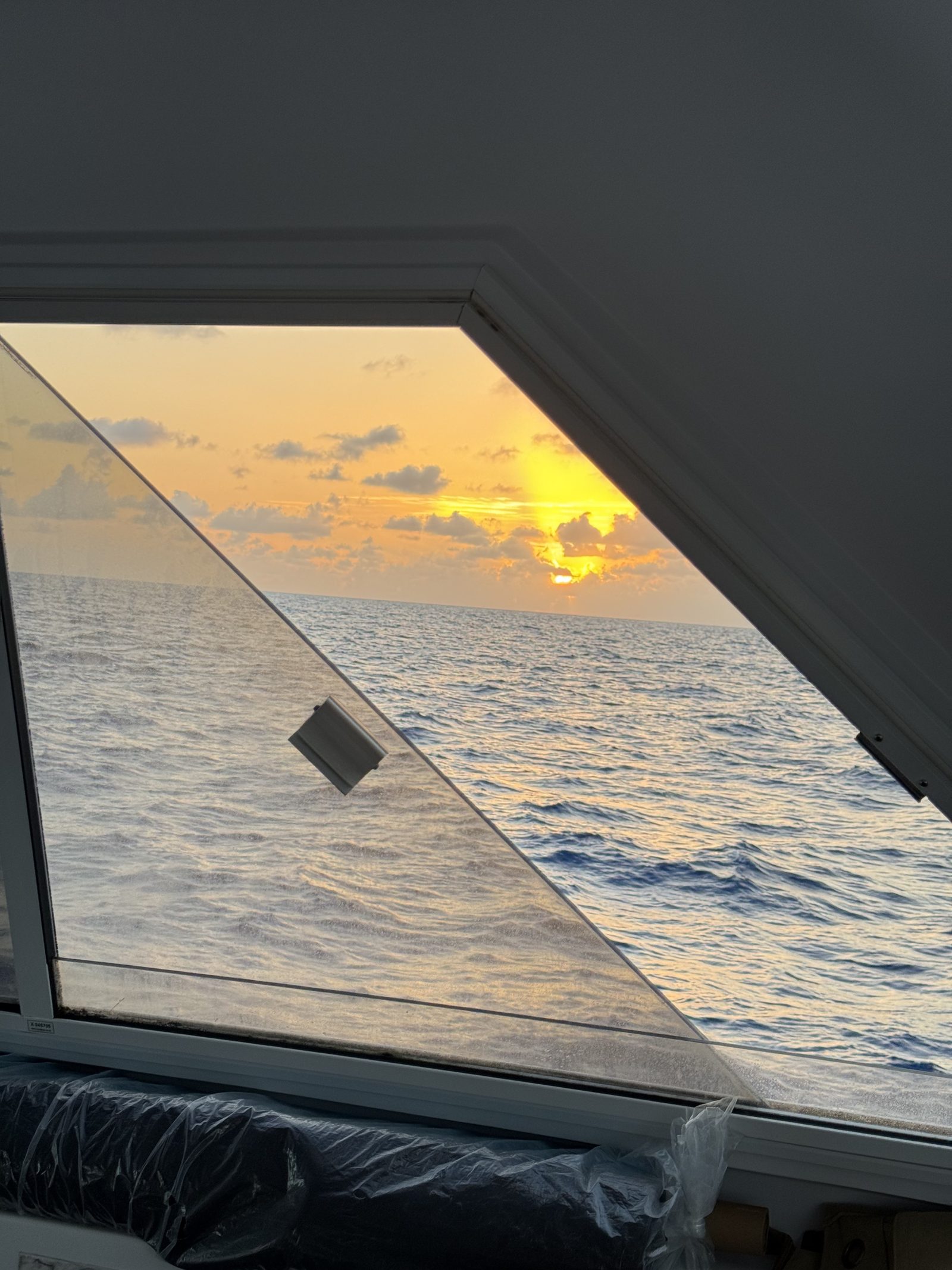 Sunrise over the ocean seen through the angled window of the catamaran.
